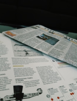 Newspapers and magazines are spread out, with text and images visible on the pages. One page has an article about historical topics, including a photo of an aircraft and a section discussing the inauguration of a political monument.
